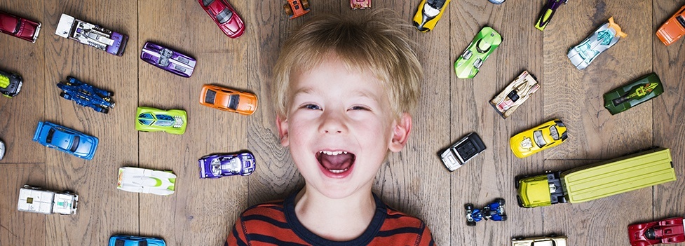 Smiling young boy surrounded by toy cars