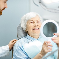 A dentist shows an older woman her new dental implants while she holds a handheld mirror
