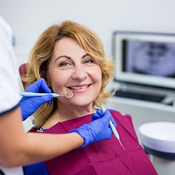 An older woman smiles while the dentist prepares to examine her smile to determine if she’s eligible for implants