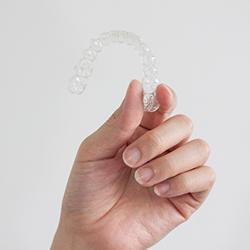 Patient holding clear aligners against light grey background