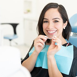 Woman smiling while holding clear aligners in dental chair